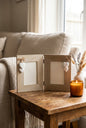 Two rustic wooden photo frames on a shelf, one labeled 'MUM' and one labeled 'DAD', each with two white heart decorations and a small piece of burlap. The frames display black-and-white family photographs, with greeting cards partially visible below on a wooden surface.