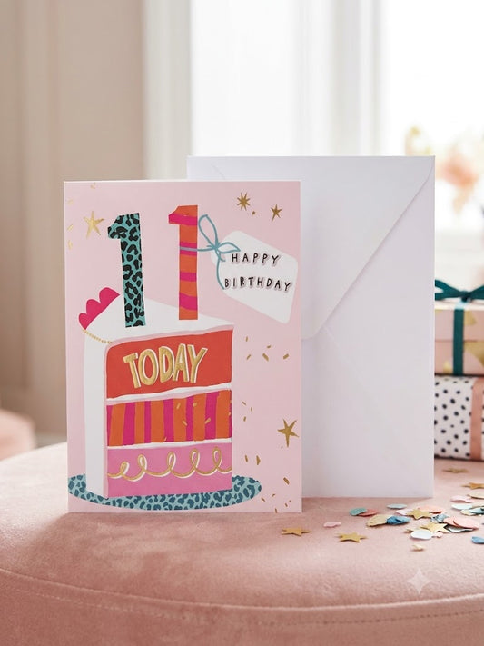 11th birthday card with illustrated cake slice, leopard print candles and gold stars on pink background with white envelope
