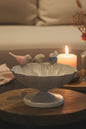 A white ceramic pedestal bowl with a scalloped rim, decorated with three small pastel birds perched on the edge, displayed on a round wooden surface.