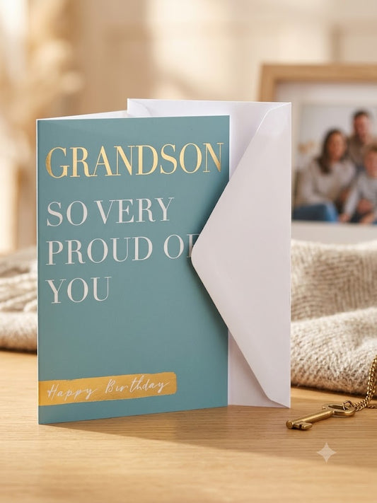 Grandson So Very Proud of You birthday card lifestyle — teal card upright with white envelope, warm natural light background