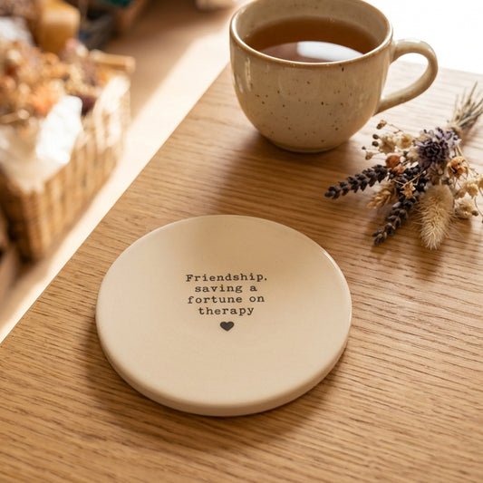 Round coaster with the words Friendship, saving a fortune on therapy and a small black heart
