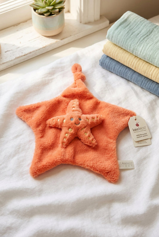 Orange Kaloo star-shaped comforter with a smiling plush starfish and pale yellow embroidered spots.
