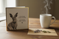 Another Grey Hare card standing open spine-left in a cosy lifestyle setting