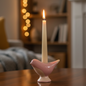 Pink ceramic bird candle holder with lit taper candle in a cosy home setting