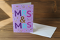 Mrs and Mrs lilac wedding card standing upright spine-left slightly open in a cosy lifestyle setting