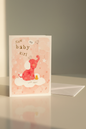 New Baby Girl card lifestyle shot – upright with white envelope, warm natural light