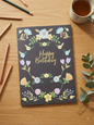 Happy Birthday card with gold foil script and pastel floral wreath on a charcoal background