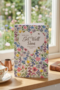 Hope You Get Well Soon card with a stunning wildflower meadow heart design featuring bees and butterflies, displayed on a windowsill with a teacup and copper watering can with a garden view