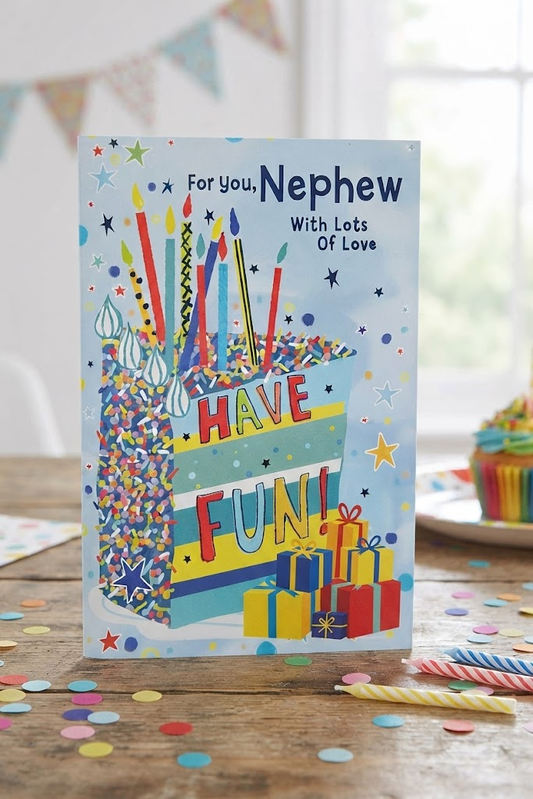 For You Nephew With Lots Of Love birthday card featuring a colourful birthday cake with candles, gifts, stars and confetti on a bright blue background, displayed on a wooden table with confetti and birthday candles