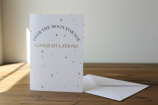 Over the Moon Congratulations gold stars card standing upright spine-left slightly open in a cosy lifestyle setting