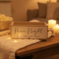 A rectangular wooden sign box with 'Movie Night' written in elegant black script, styled on a wooden table with a knitted blanket, string lights, popcorn, and candles in a cozy living room setting.