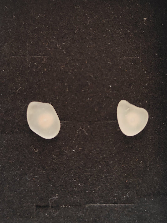A pair of small, irregularly shaped off-white translucent stones or beads displayed inside a white presentation box with a black velvet insert, set on a dark gray tabletop.